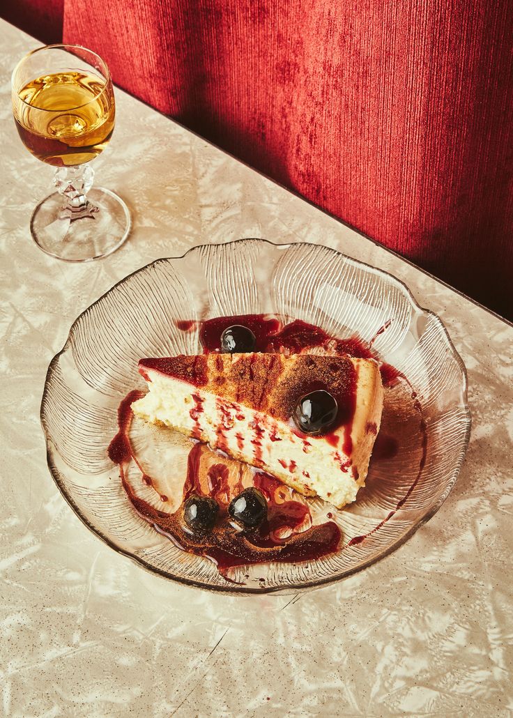 a piece of cheesecake on a glass plate next to a wine glass and bottle