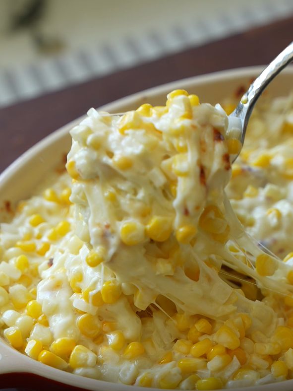 a spoon with some food in it on top of a bowl filled with corn and coleslaw