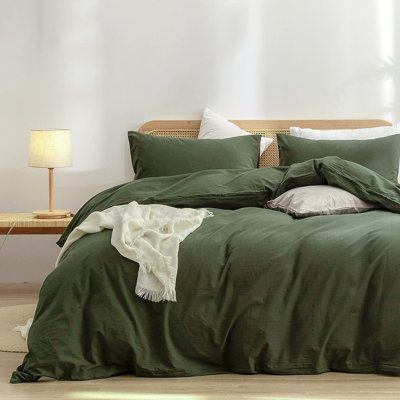 a bed with green sheets and pillows in a white room next to a wooden bench