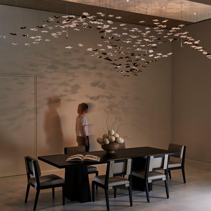 a woman standing in front of a dining room table with many butterflies hanging from the ceiling