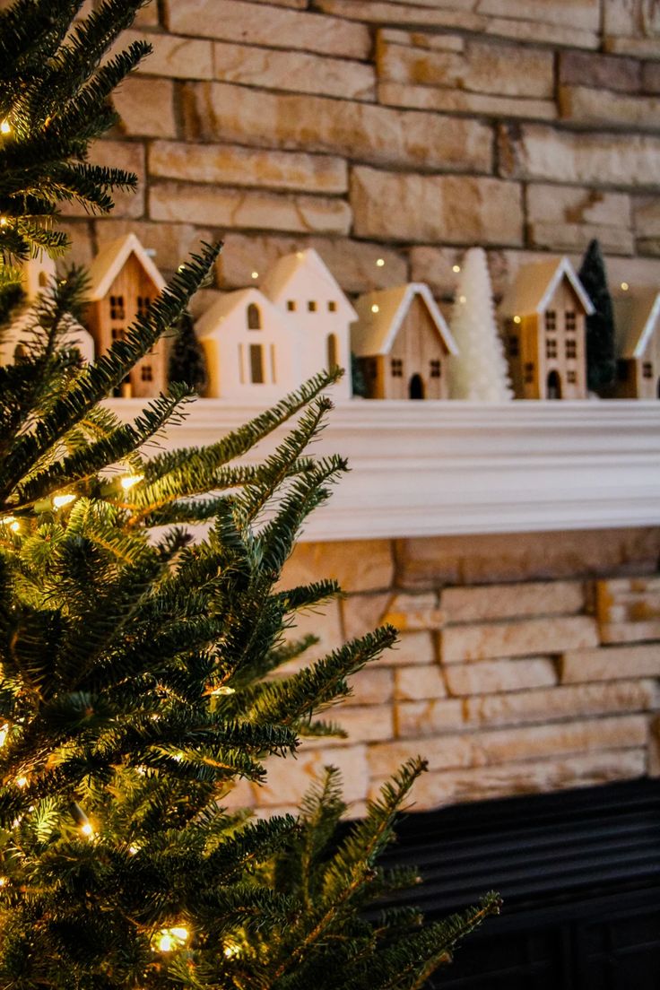 a small christmas tree is next to a brick wall with houses on it and lights