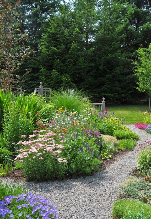 a garden filled with lots of different types of flowers and plants on top of gravel