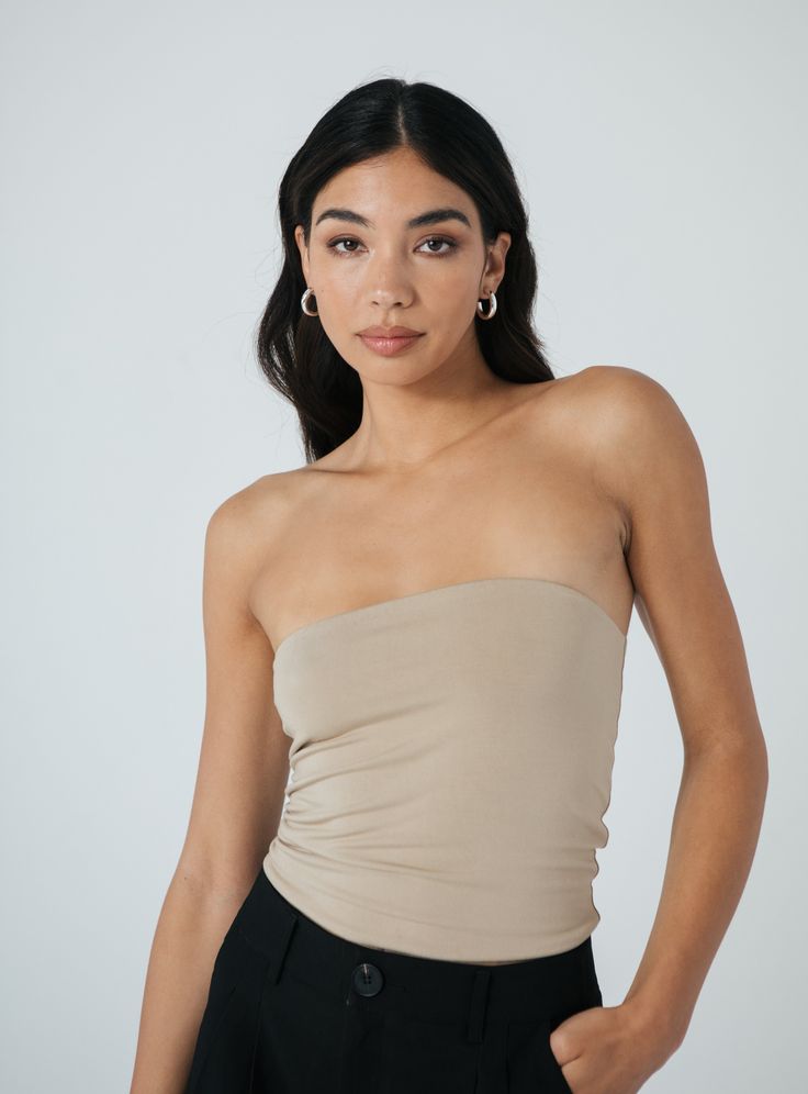 a woman wearing a tan tube top and black pants with her hands on her hips