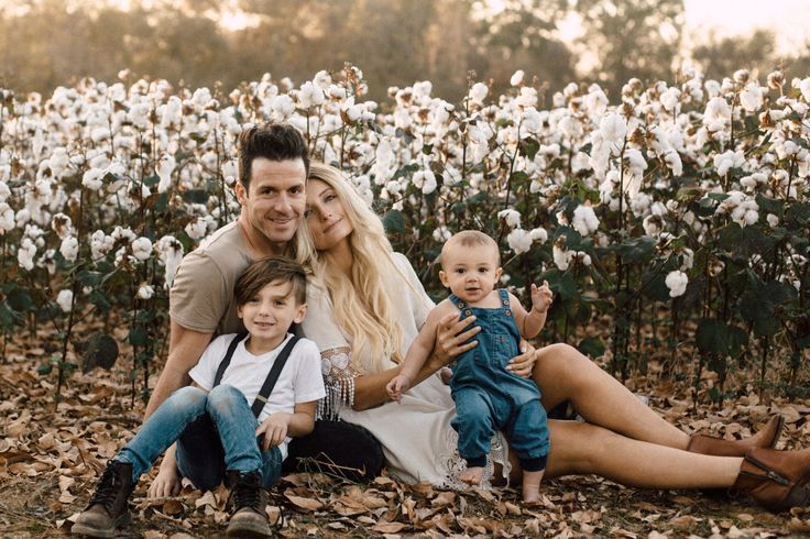 a man, woman and two children sitting on the ground in front of a cotton field