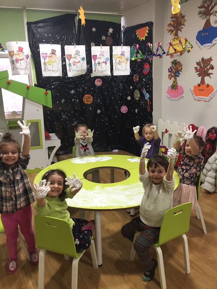 several children sitting around a green table and chairs in a room with decorations on the walls