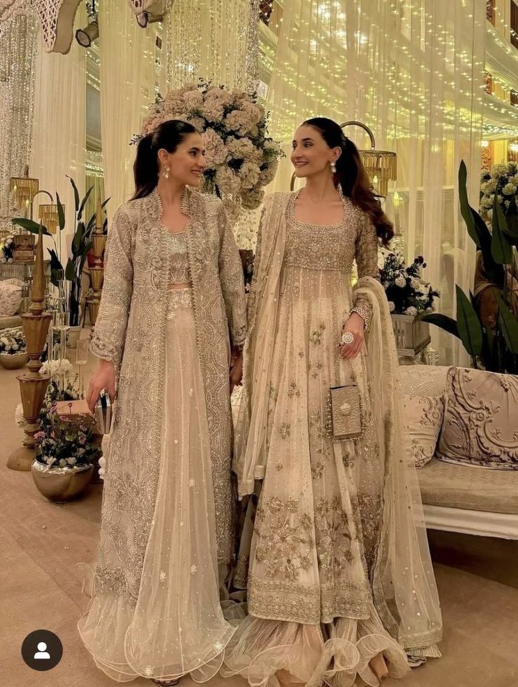 two women standing next to each other in front of a white couch and chandelier