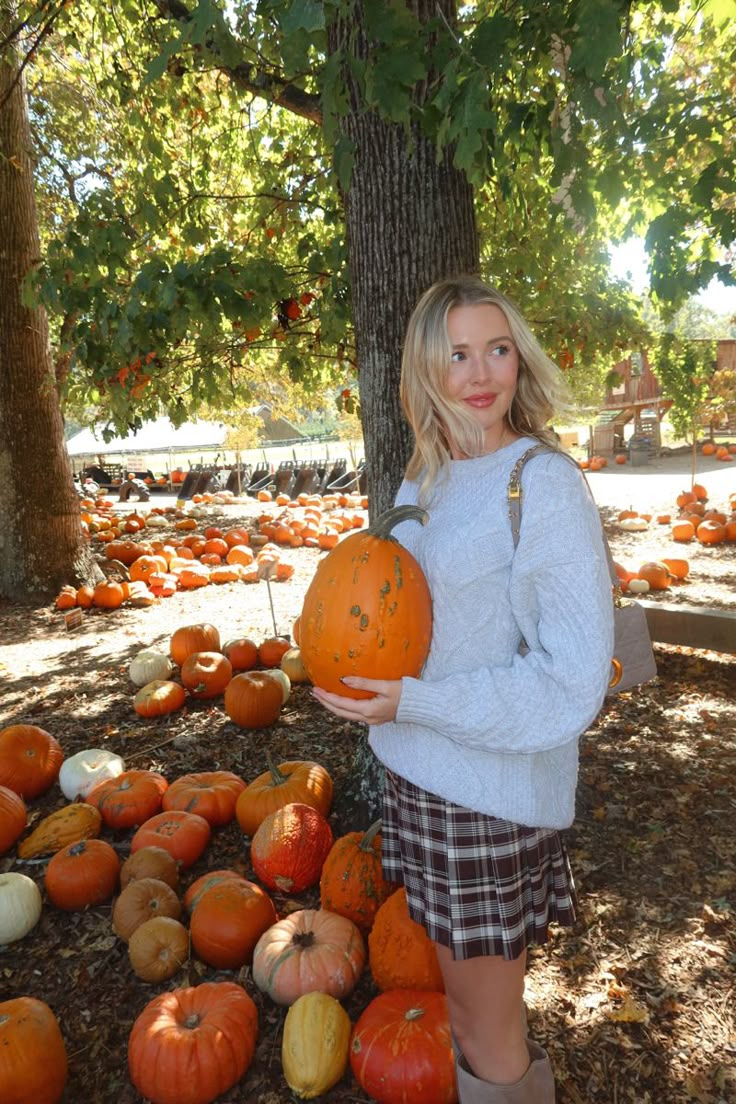 a woman standing in front of a pile of pumpkins