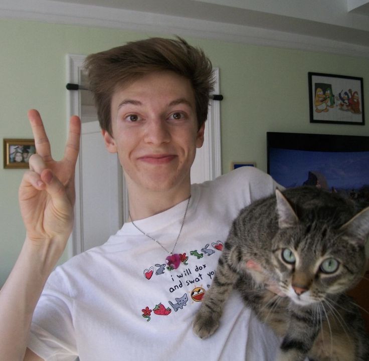 a man holding a cat in his arms and making the peace sign with both hands