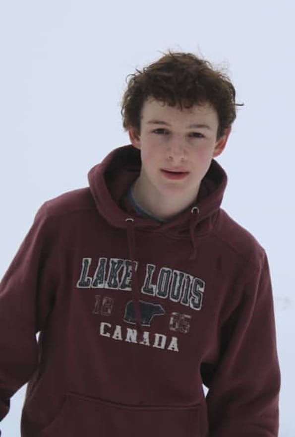 a young boy standing in the snow wearing a maroon hoodie that says lake louis is canada