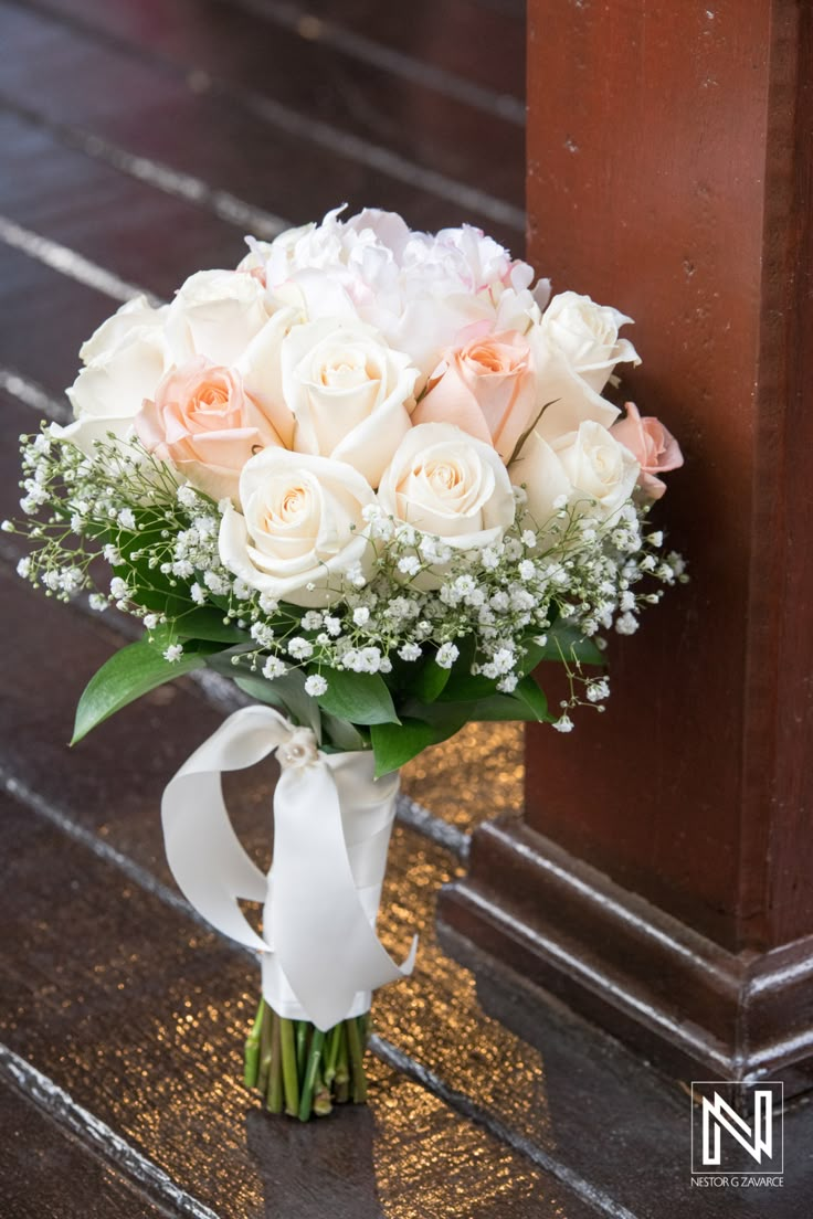 a bouquet of white and pink roses on the ground next to a wooden door with ribbon