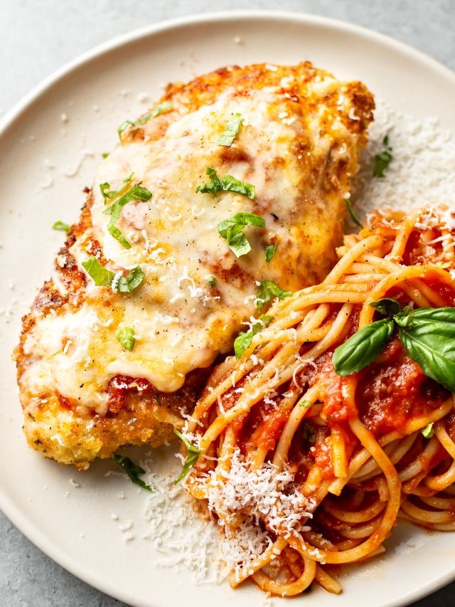 two pieces of chicken parmesan and pasta on a white plate with basil garnish