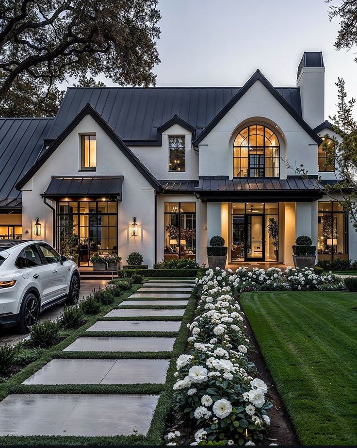 a white car is parked in front of a large house with lots of windows and landscaping