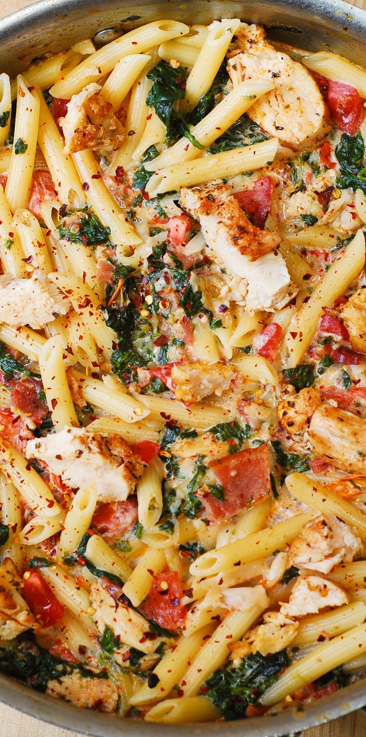 a pan full of pasta with chicken and spinach on top, sitting on a table