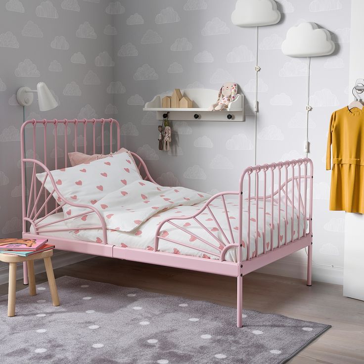 a child's bed with pink metal frame and white sheets in a bedroom setting