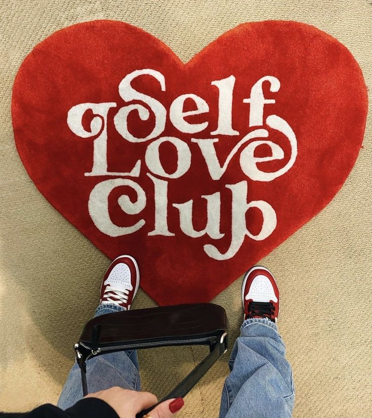 someone holding a red heart shaped pillow with the words self love club on it