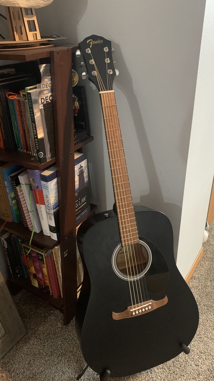 a black acoustic guitar sitting on top of a wooden stand next to a book shelf