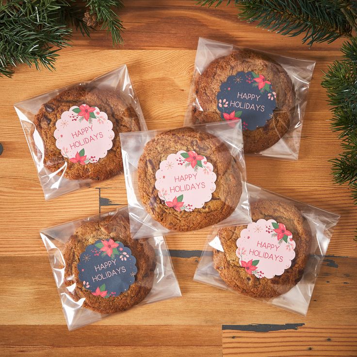 four cookies wrapped in plastic on top of a wooden table next to christmas tree branches