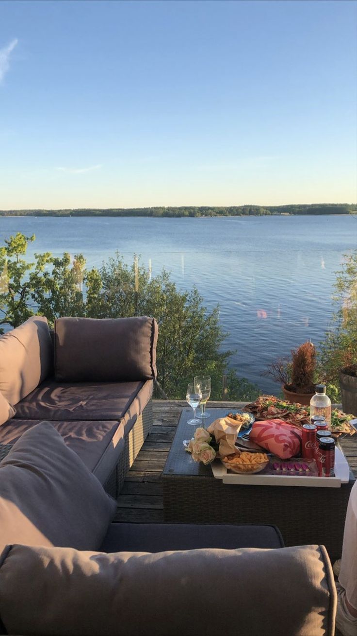 a couch and table with food on it by the water in front of some trees