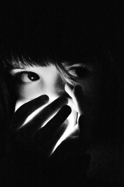 black and white photograph of a woman covering her face with both hands in the dark