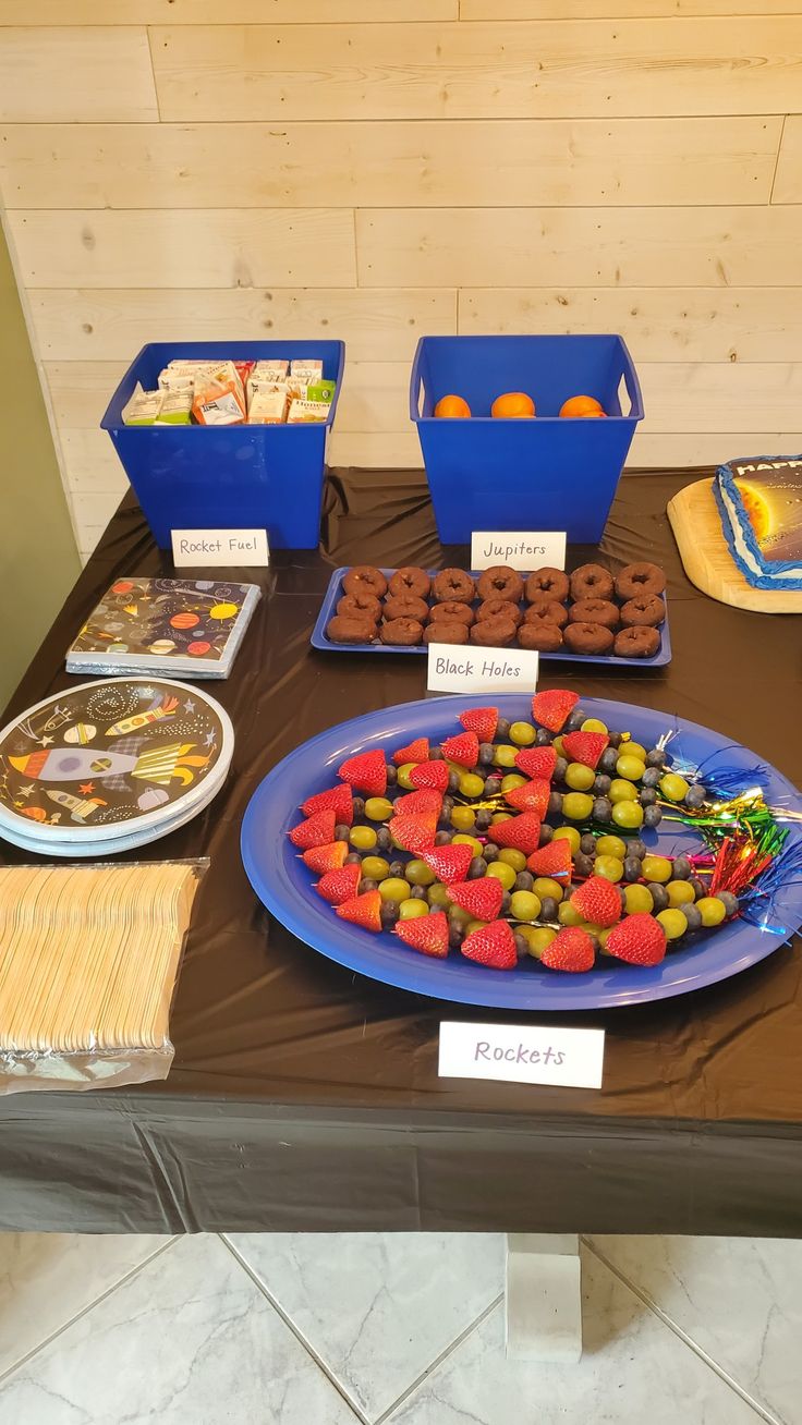 a table topped with plates and trays filled with food next to boxes of fruit