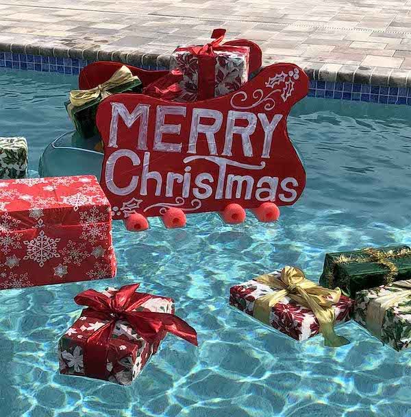 christmas presents floating in a pool with merry sign and decorations on it's side