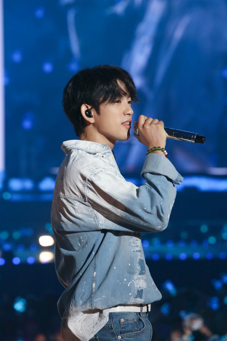 a young man holding a microphone in his right hand while standing next to an audience