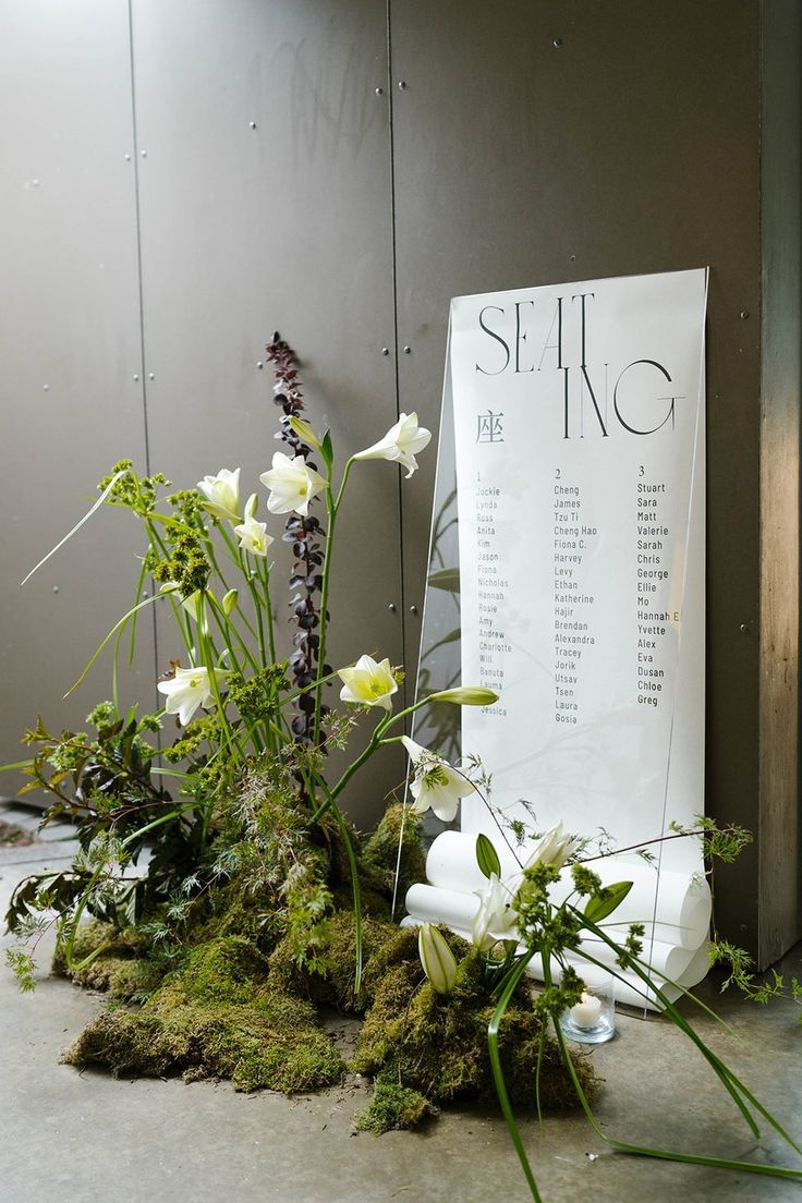 an arrangement of flowers and moss in front of a sign