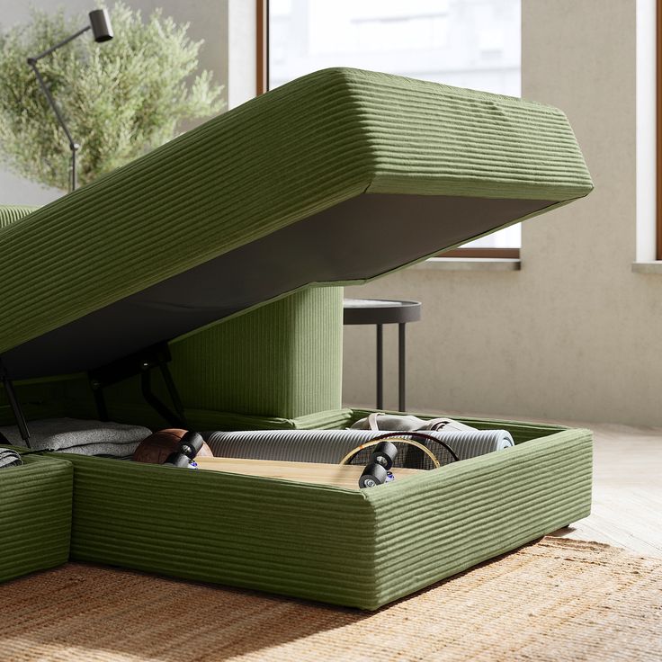 an open green bed sitting on top of a wooden floor next to a table and window