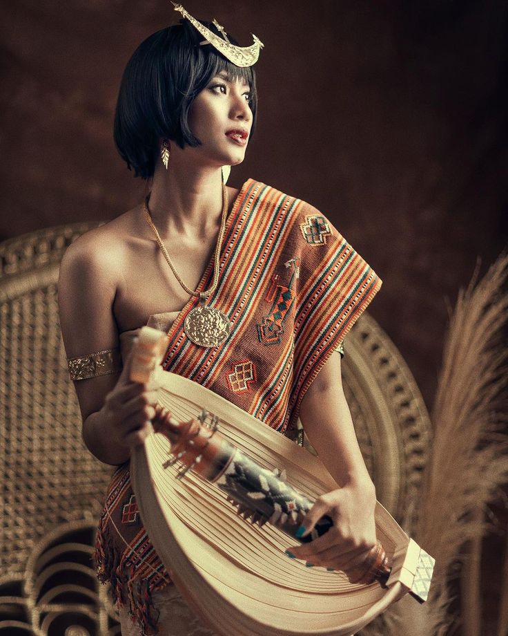 a woman in an orange and gold dress holding a wooden plate with feathers around her neck