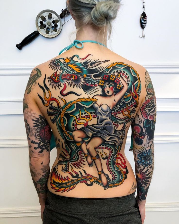 a woman with tattoos on her back standing in front of a wall