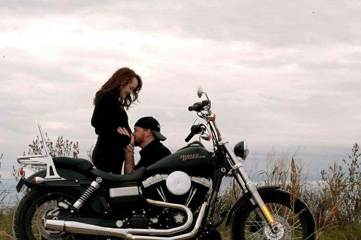 a man and woman standing next to a motorcycle