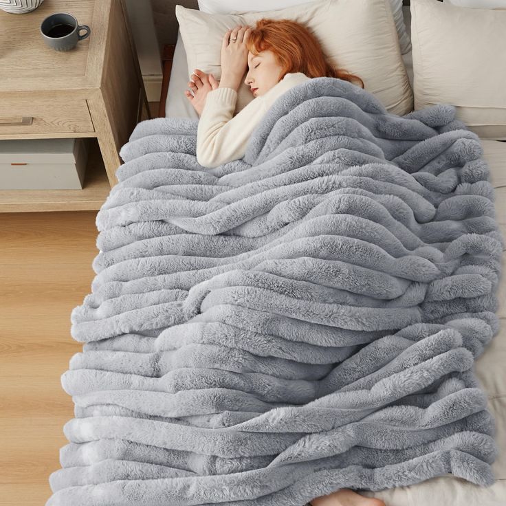 a woman laying in bed under a fluffy blanket