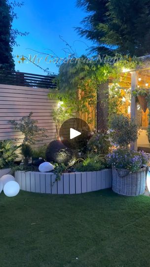 an outdoor garden with lights and plants in the center, surrounded by white round planters