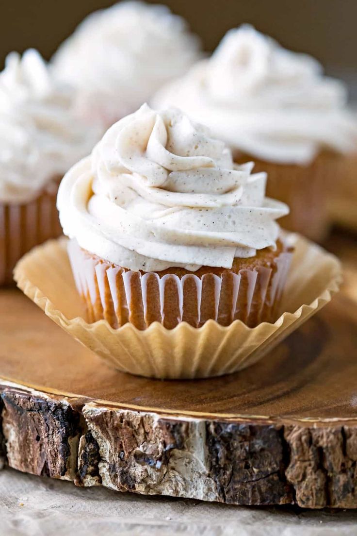 cupcakes with white frosting sitting on a wooden plate