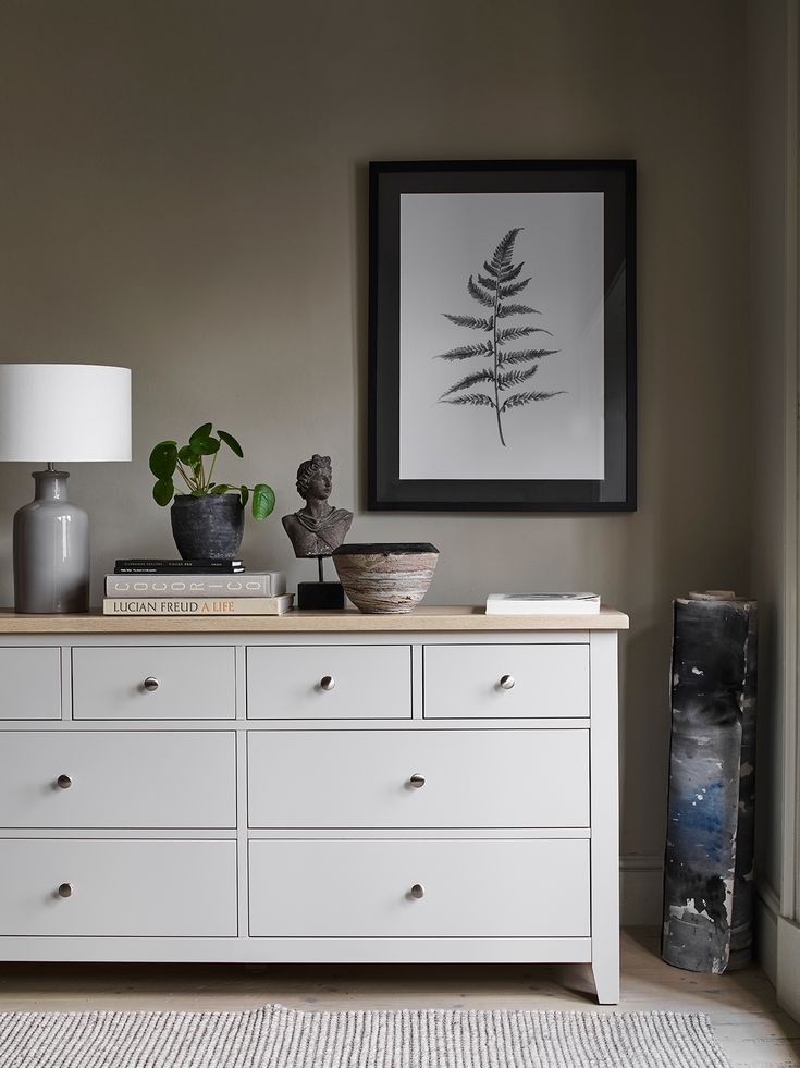 a white dresser with two vases on top of it next to a framed plant