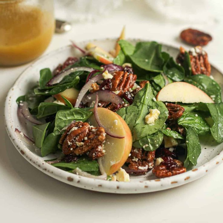 a white plate topped with spinach salad and apples