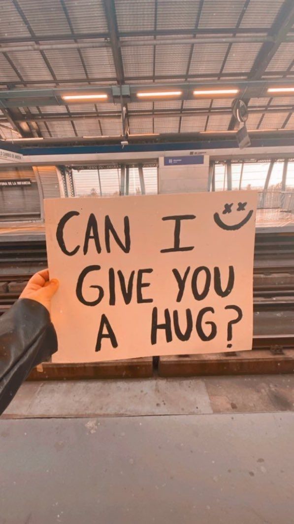 a person holding a sign that says can i give you a hug?