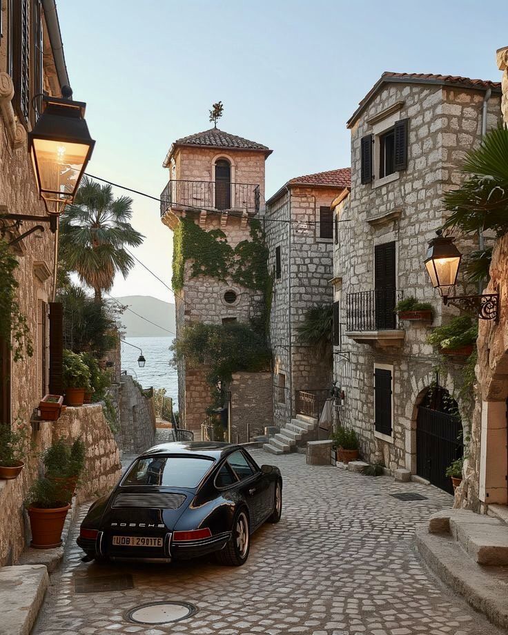 a black car parked on the side of a cobblestone street next to stone buildings