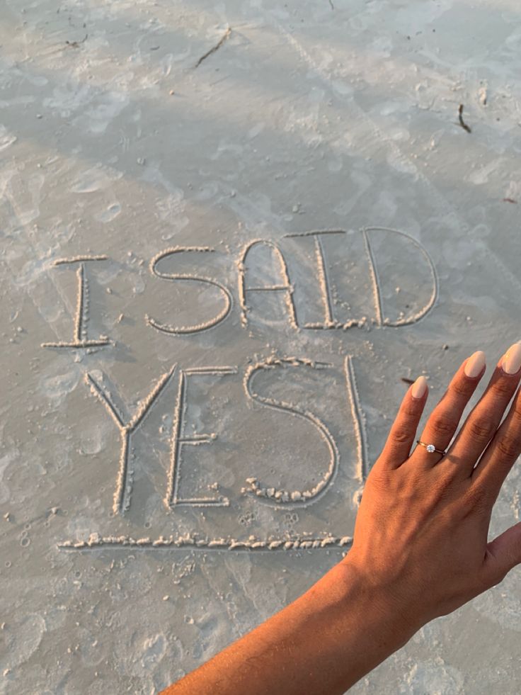 a woman's hand writing i said yes in the sand