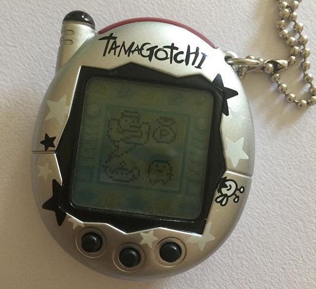 an electronic device is hanging on the wall next to a ball chain necklace that says tamagotchi