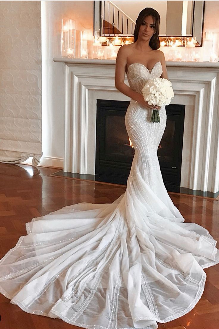 a woman standing in front of a fireplace wearing a wedding dress and holding a bouquet