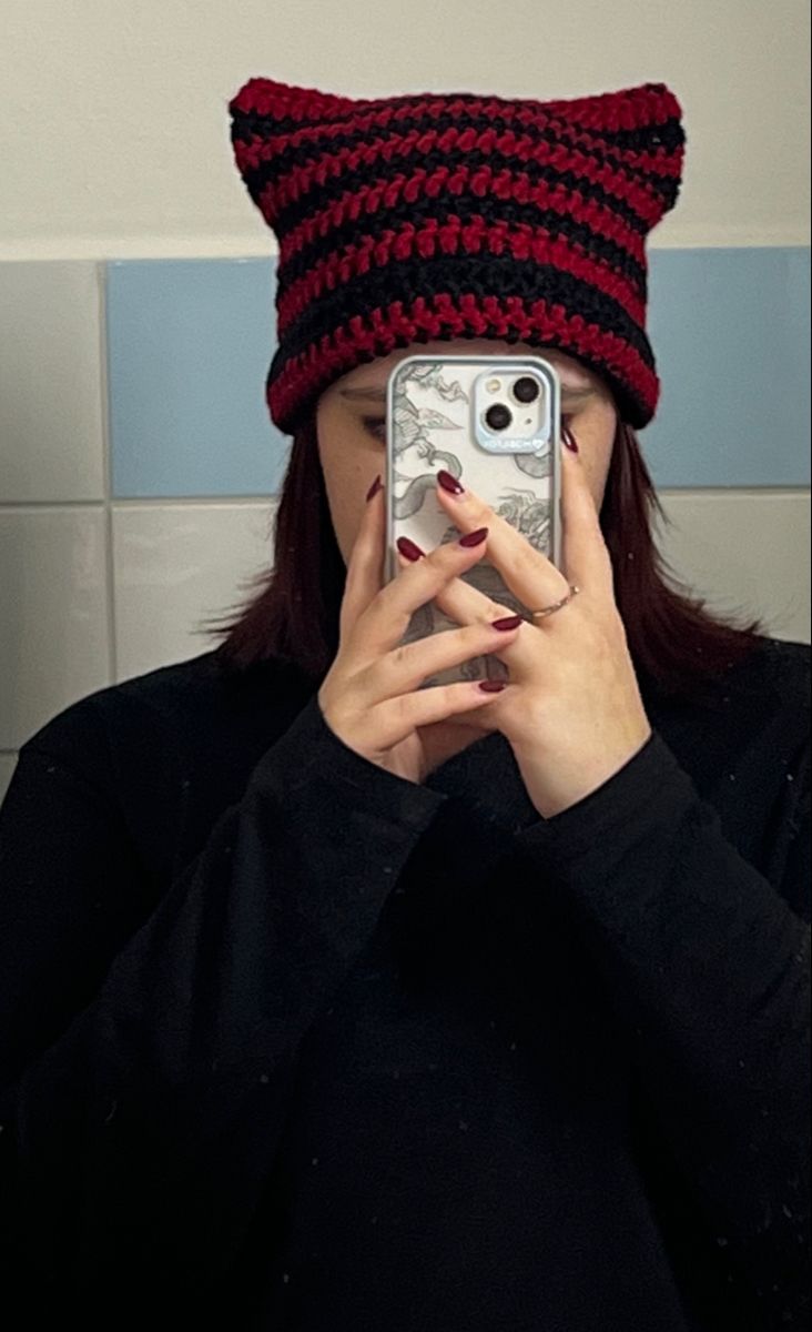 a woman taking a selfie in front of a mirror wearing a knitted cat hat