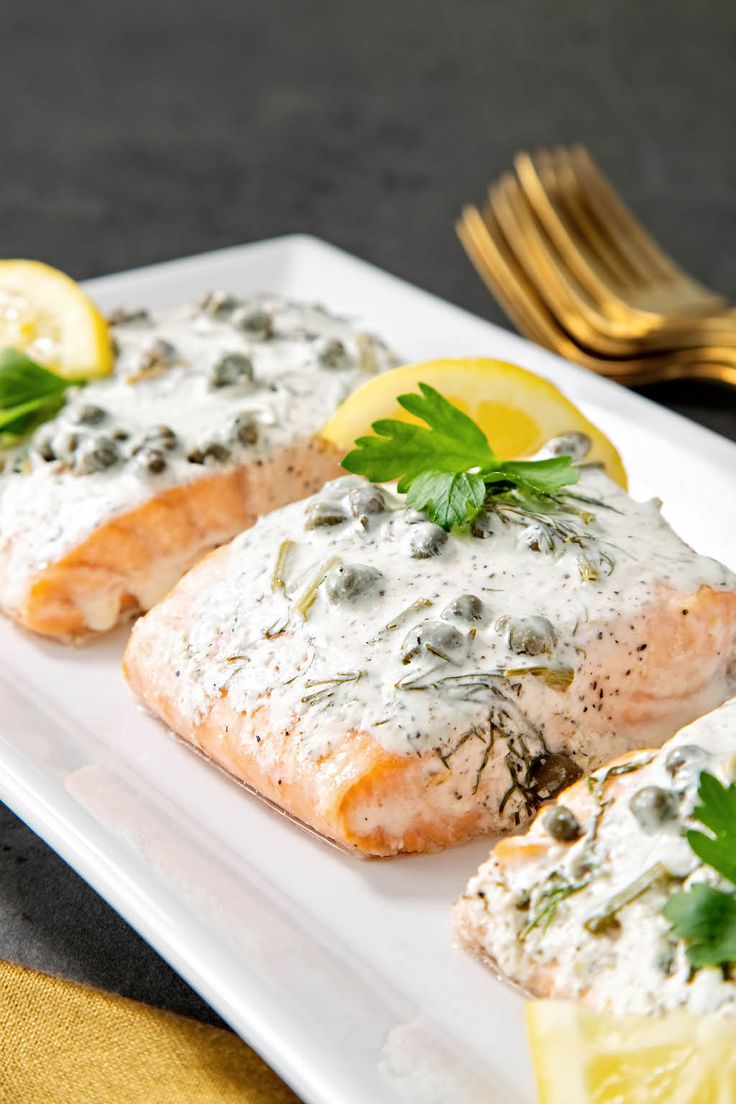 two salmon fillets on a white plate with lemon wedges and green garnish