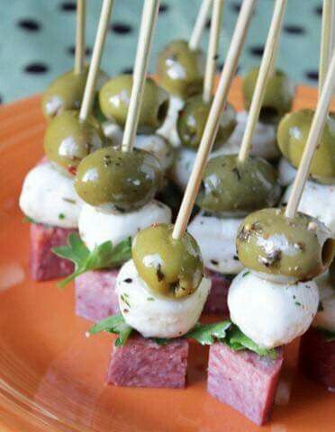 small appetizers with olives and meat on skewers are displayed on an orange plate