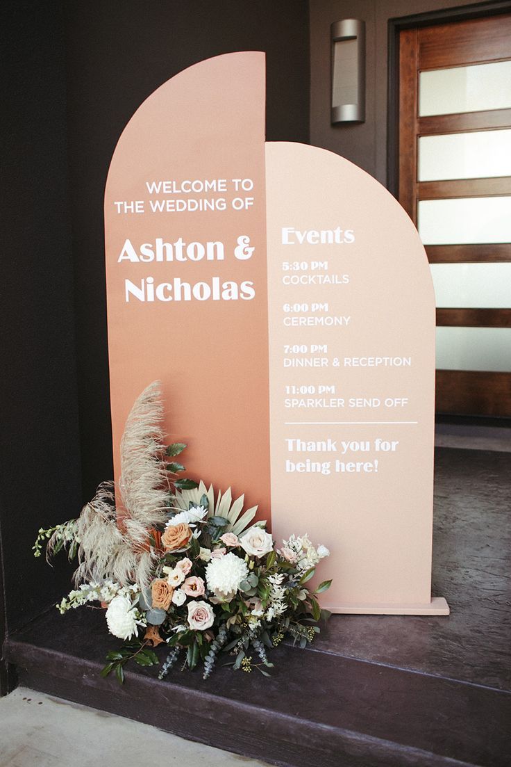 a welcome sign with flowers and greenery in front of it on the steps to an entrance