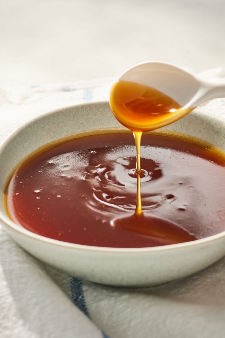 a spoon pouring sauce into a bowl on top of a white cloth with a blue and white towel