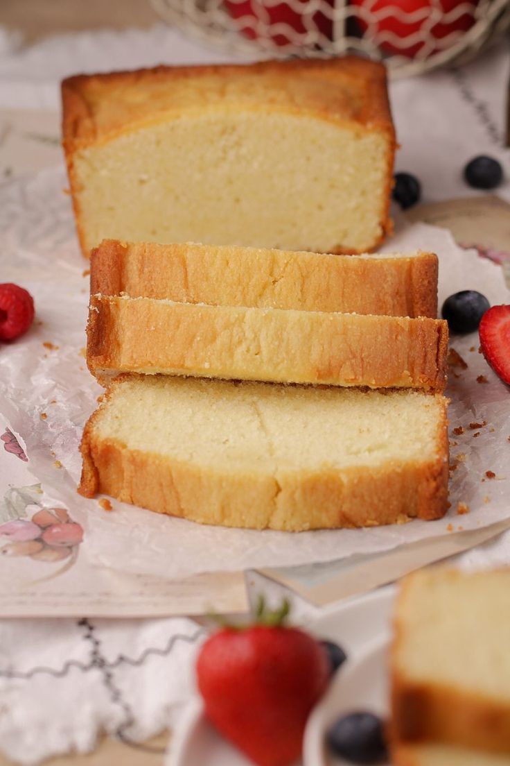 two slices of pound cake sitting on top of paper next to strawberries and blueberries