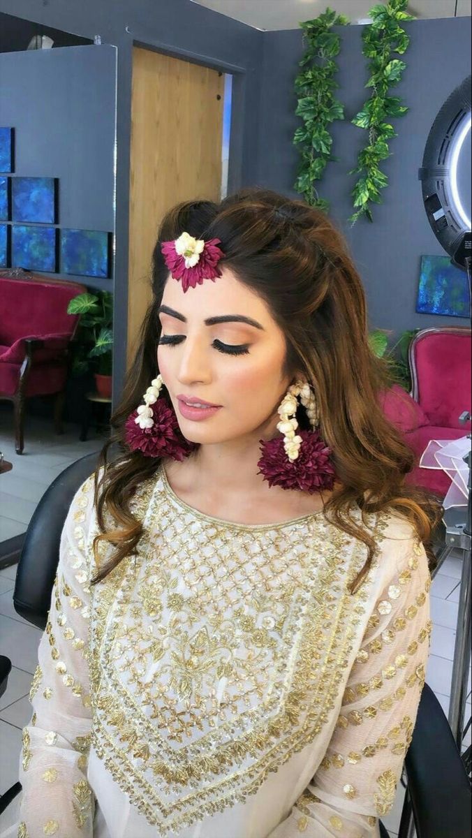 a woman sitting in front of a mirror wearing flower earrings and a white dress with gold sequins