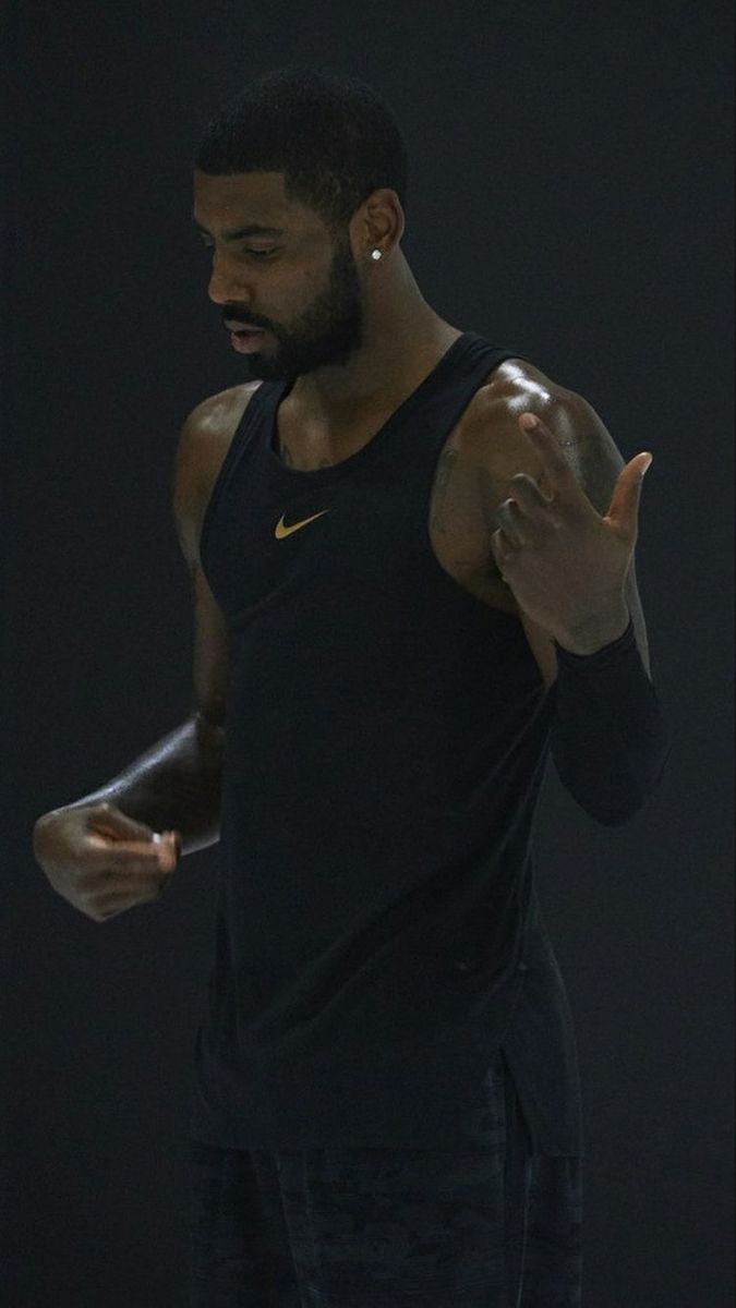 a man standing in the dark with his hand up and wearing a black tank top