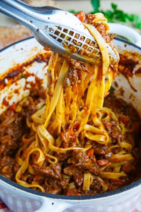 spaghetti being lifted from a pot with meat sauce and parmesan cheese on top